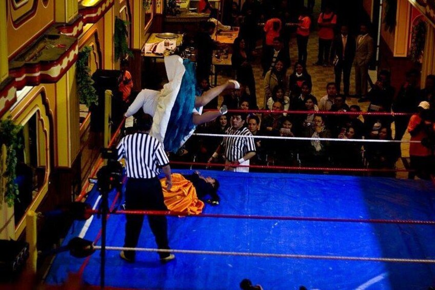 Un ring de lucha libre con dos árbitros y una multitud en un espacio interior amplio. 3