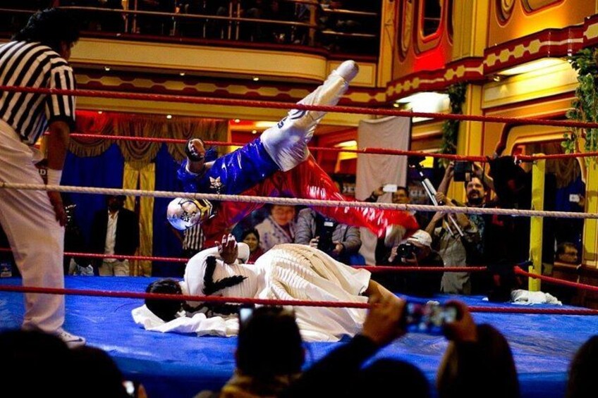 A wrestling match in a ring with a referee and an audience. 1