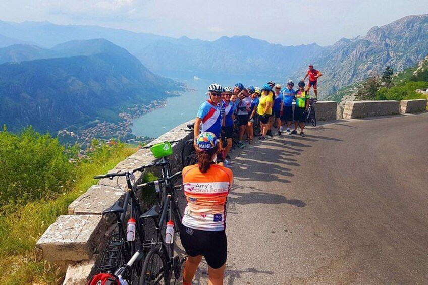 Een groep fietsers op een bergweg met een mooi uitzicht op een meer en bergen op de achtergrond. 5