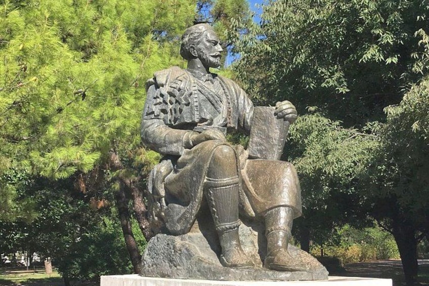 A statue of a seated figure with a book, surrounded by trees. 1