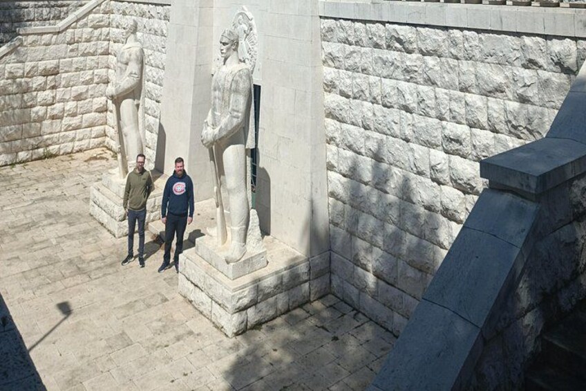 Two people standing near ancient stone statues in a courtyard. 2