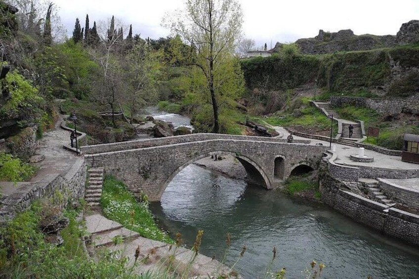 A stone bridge over a river, surrounded by greenery and stone walls. 5