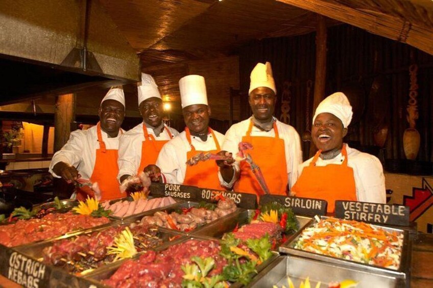 Cocineros con gorros blancos y delantales naranjas detrás de un bufé con secciones de comida identificadas. 1