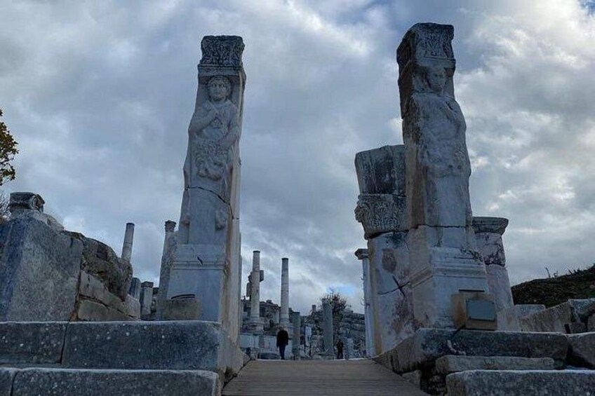 Ancient stone pillars with carvings, a pathway leading through ruins, and a cloudy sky. 3