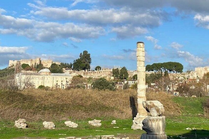 Ancient ruins with a tall column, a fortress in the background, and a clear sky. 5