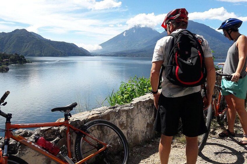 A lake with mountains in the background, a bicycle, and a person wearing a helmet. 4