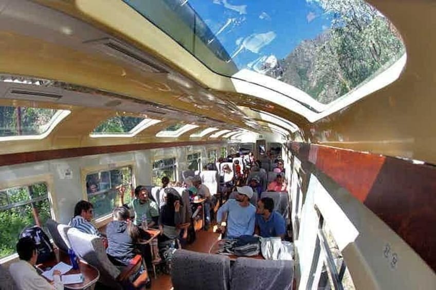 A crowded train carriage with passengers seated and standing, large windows, and a curved ceiling. 5