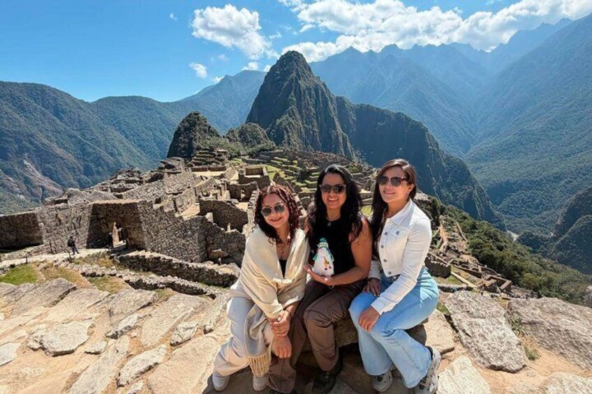 Three people sitting on a stone ledge with Machu Picchu ruins in the background. 2