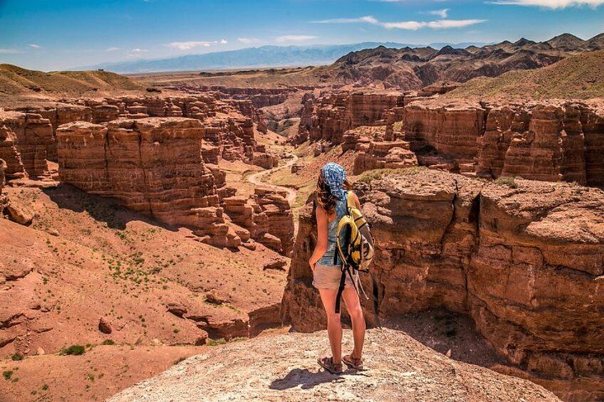 A hiker with a backpack standing on a rocky outcrop overlooking a canyon. 1