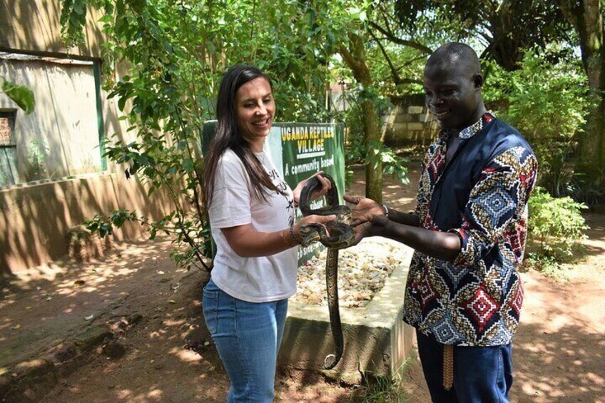 Two people holding a snake in a garden with a sign about Ugandan reptiles. 5