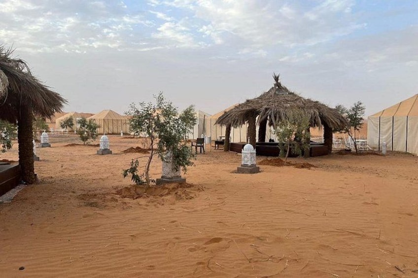 A desert landscape with tents, a thatched hut, and small trees. 1