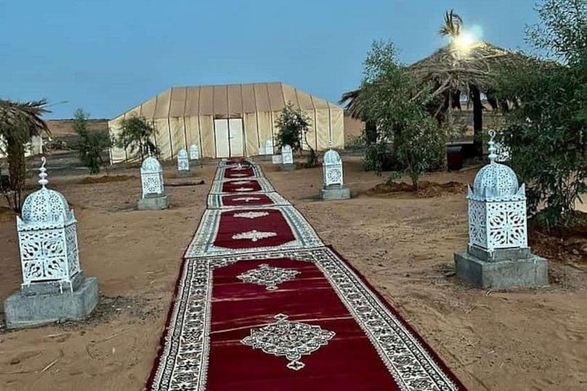 A desert pathway with a red carpet, white lanterns, and a tent in the background. 3