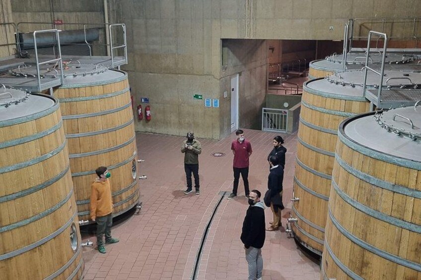 A group of people standing around large wooden barrels in an industrial setting. 4