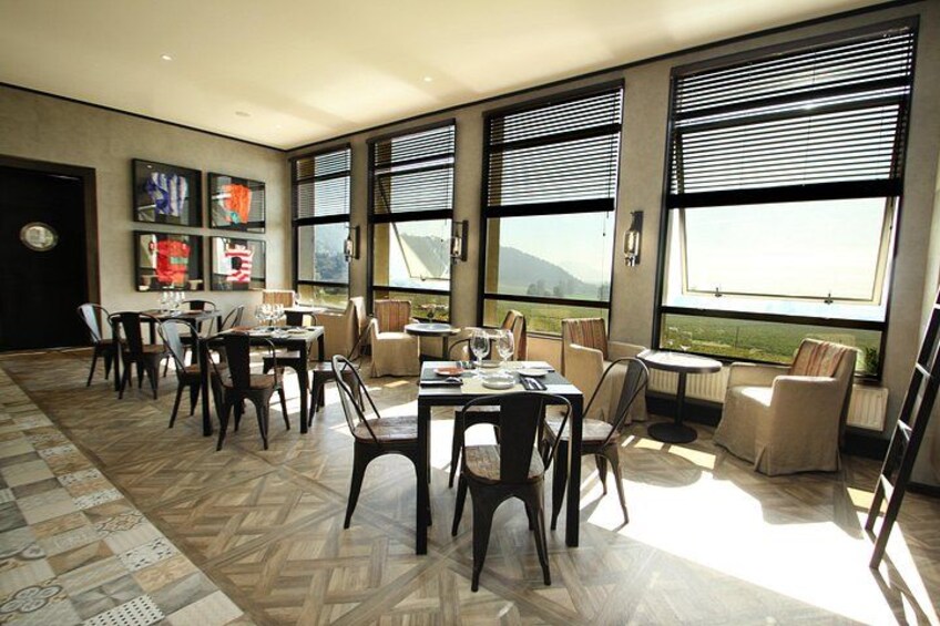 A dining area with multiple tables and chairs, large windows with blinds, and a view of the outdoors. 2