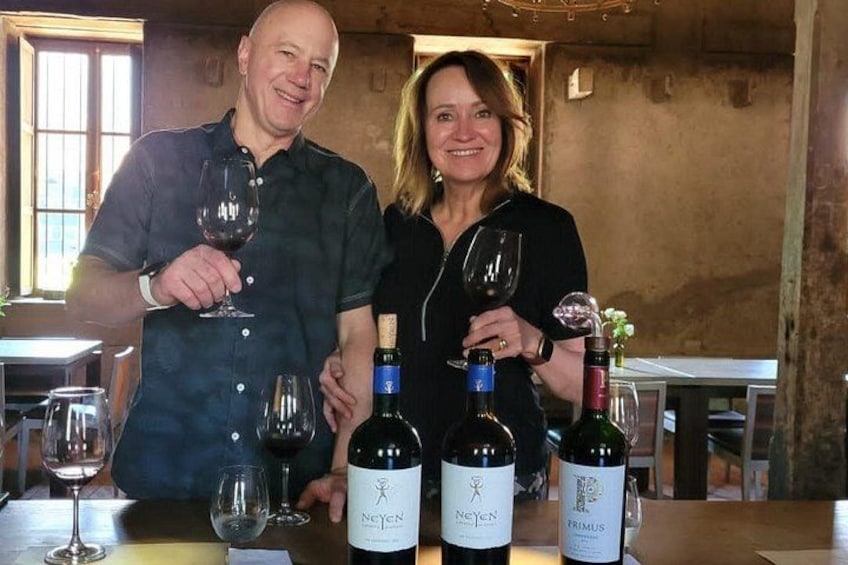 Two people standing at a bar with wine bottles and glasses. 4