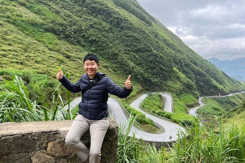 A person sitting on a rock with a mountainous landscape and winding roads in the background. 2