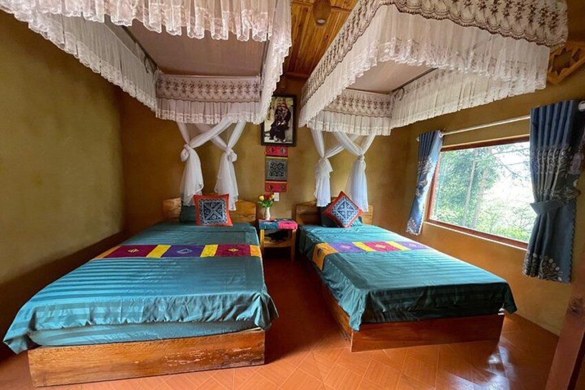A room with two beds, a wooden floor, a window with curtains, and a decorative canopy. 5