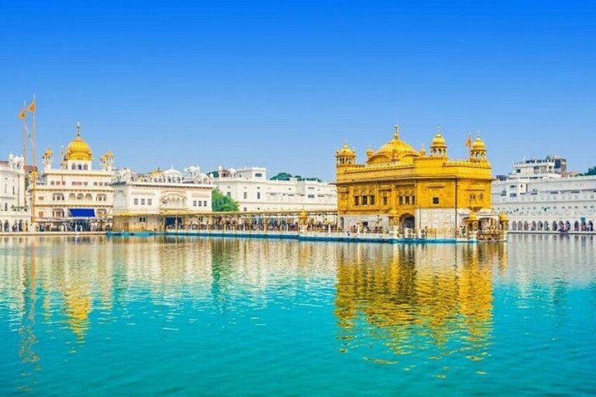 The Golden Temple with a reflection in the water, surrounded by white buildings and a clear blue sky. 1