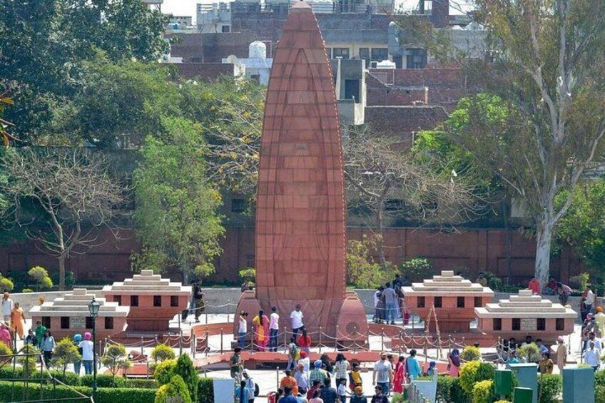 A large obelisk monument surrounded by a crowd of people in a park with trees and buildings in the background. 4
