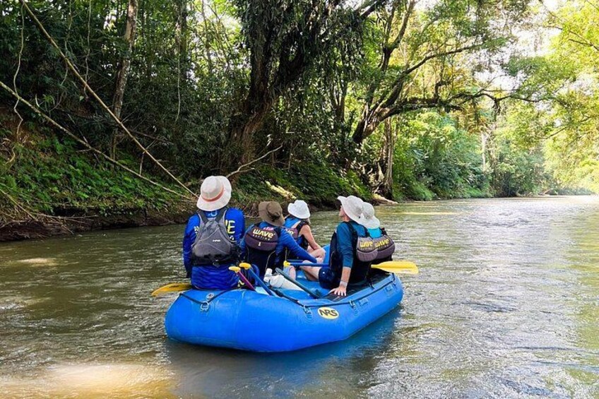Eine Gruppe von Menschen in einer blauen Floß auf einem Fluss, umgeben von dichtem Grün. 2