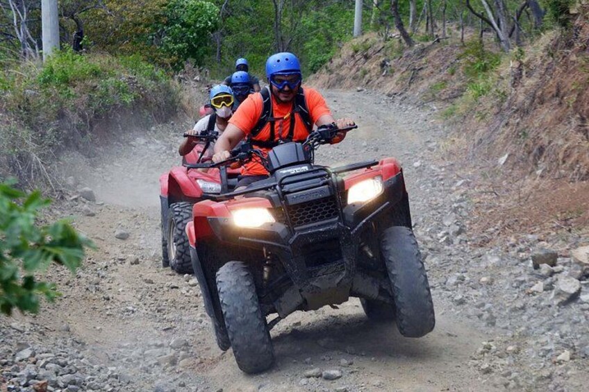 Three people riding ATVs on a dirt trail surrounded by trees. 2