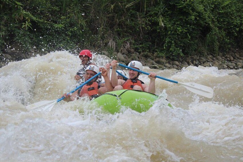 People in a green raft navigating a turbulent river surrounded by dense greenery. 2