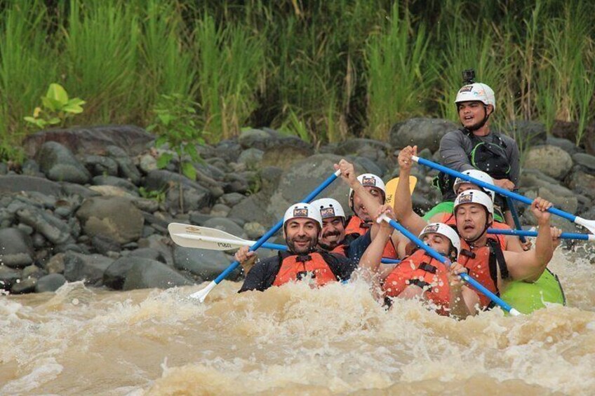 A group of people in a green raft navigating a river with rocks and rapids. 5