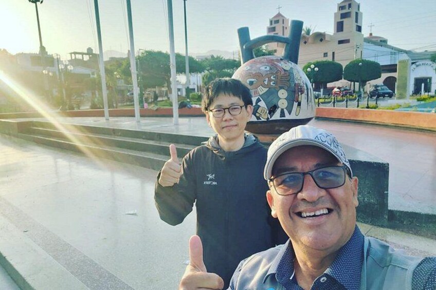 Two people giving a thumbs-up gesture, a large decorative sculpture, and a building with a cross on top in the background. 5