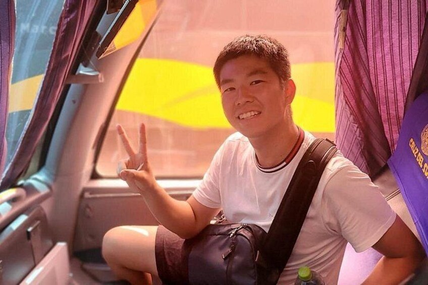 A person sitting in a vehicle with a backpack, making a peace sign. 4