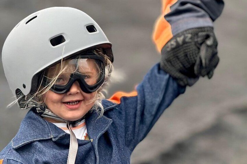 A child wearing a helmet and gloves, raising their hand. 5