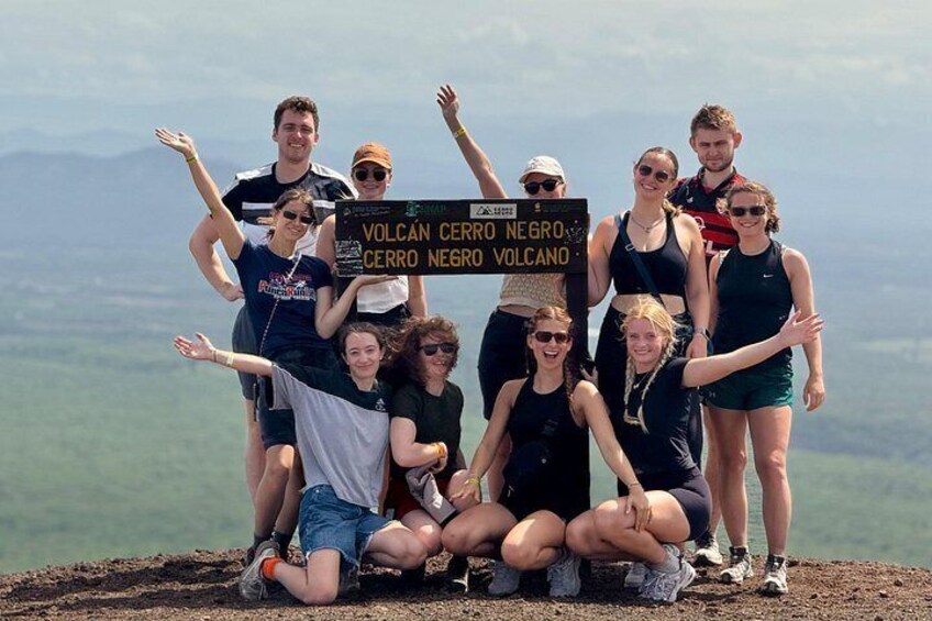 A group of people posing with a sign on a volcanic peak. 2