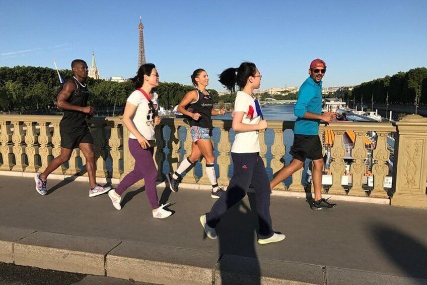 A group of people jogging on a bridge with a river and a tower in the background. 3