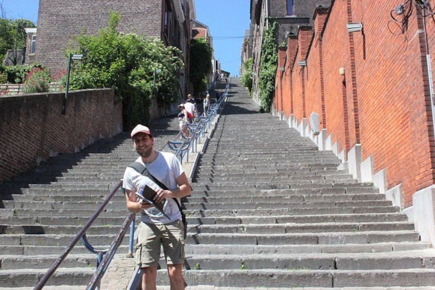A person descending a set of stone stairs with metal railings, surrounded by brick buildings and greenery. 5