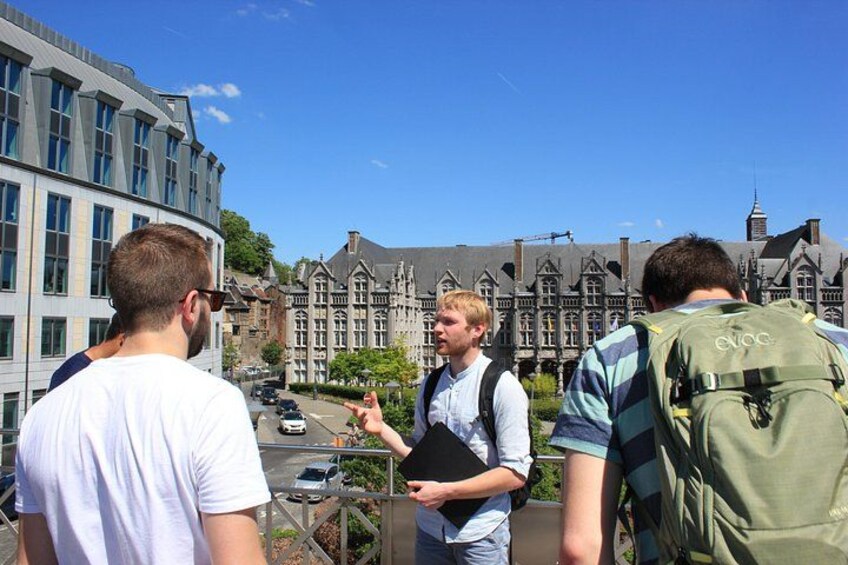 Three people standing on a balcony overlooking a historic building with multiple windows and a clear sky. 1