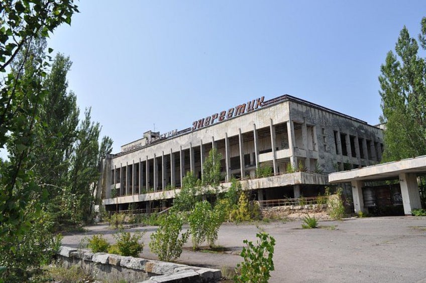 A large, multi-story building with the sign 'Soviet' on the facade, surrounded by trees and a paved area. 1