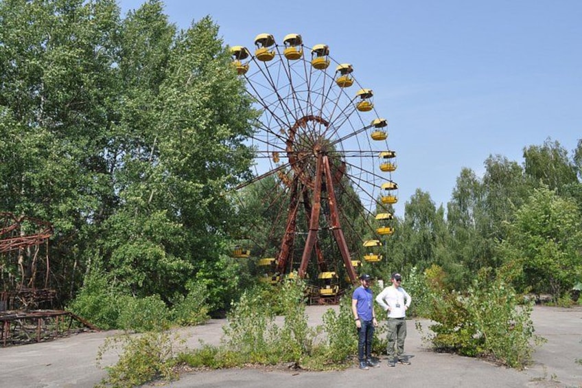 A large Ferris wheel with yellow cabins, surrounded by trees and greenery. 3