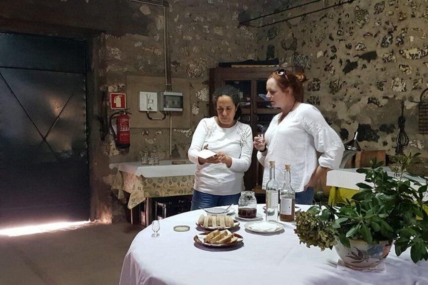 Dos personas de pie junto a una mesa con comida y bebidas, en una habitación rústica con un extintor y una planta. 2