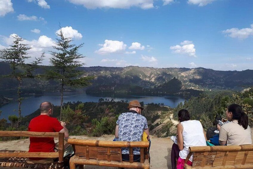 People sitting on wooden benches overlooking a lake and hills. 1