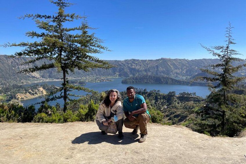 Two people posing on a rocky outcrop with a lake and mountains in the background. 2