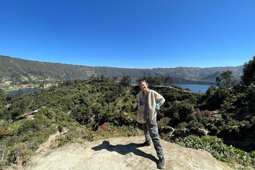 A person standing on a hill overlooking a valley with a lake and mountains in the distance. 4