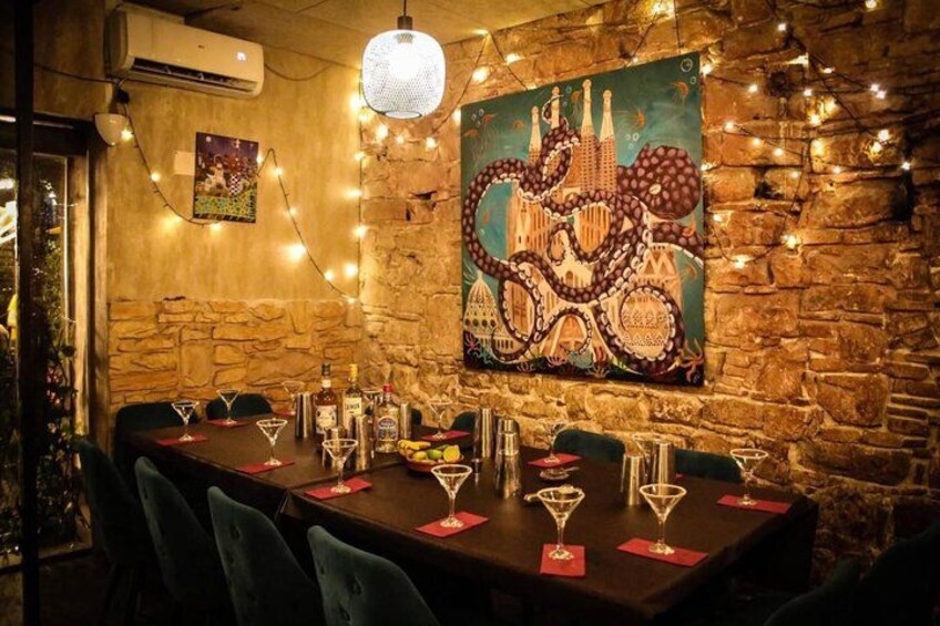 En restauranginteriör med en vägg av sten, en målning som föreställer en stadsbild, ljusslingor och ett bord dukat för en måltid. 2