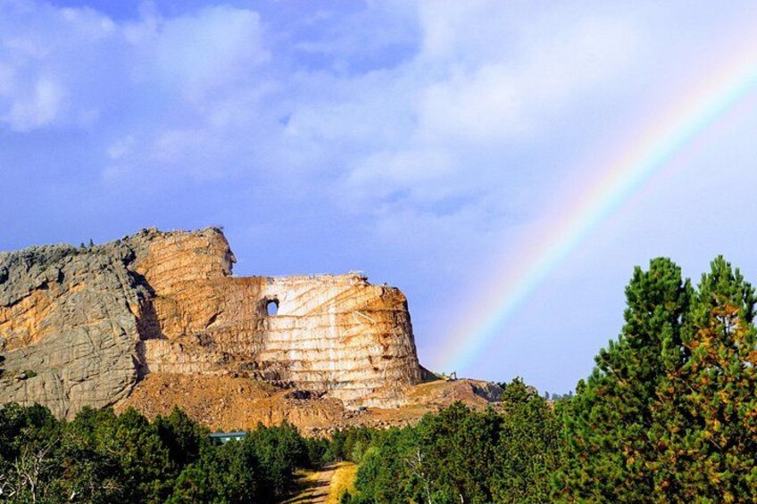 A rocky cliff with a hole, a rainbow, and dense green trees. 2