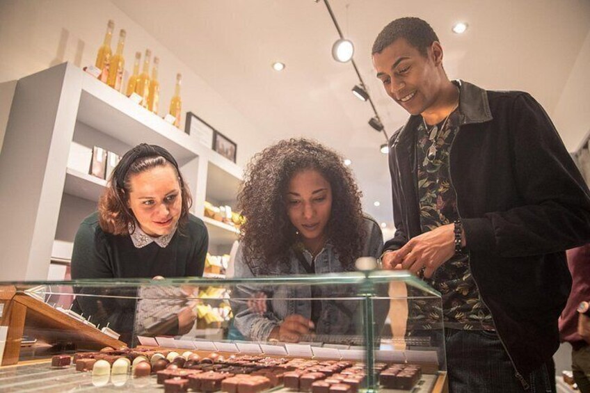 Tres personas observando chocolates en una vitrina de vidrio. 1