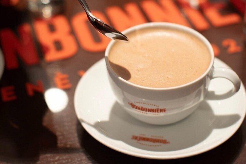 Una taza de café con una cuchara, sobre un platillo con el texto 'BONBONNIERE' y una mesa con el texto 'NBO' visible parcialmente. 2