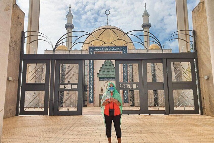 A person standing in front of a mosque entrance with a large gate and minarets. 1