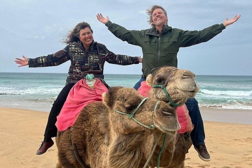 Två personer som rider på en kamel på en strand med havet i bakgrunden. 1