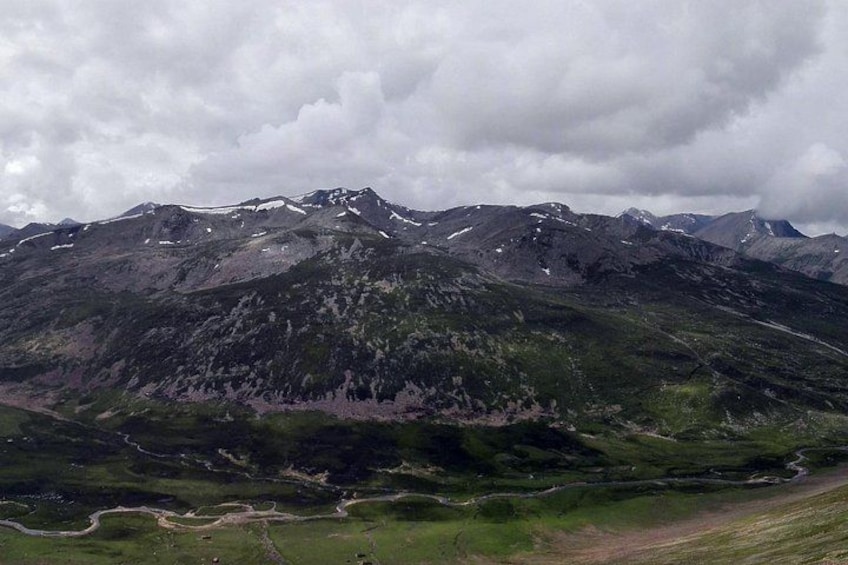 A mountainous landscape with a winding road and patches of snow on the peaks. 2