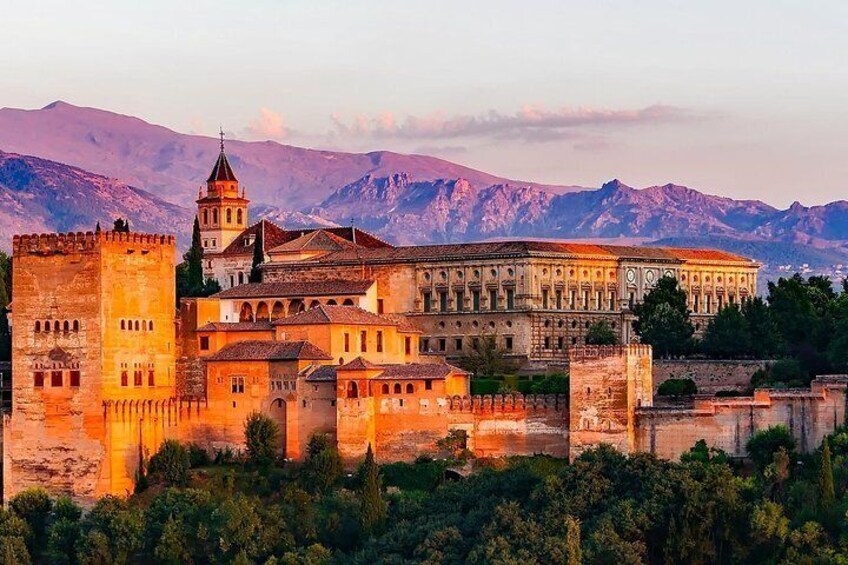 A historic building complex with a prominent tower and fortress walls, set against a mountainous backdrop. 2