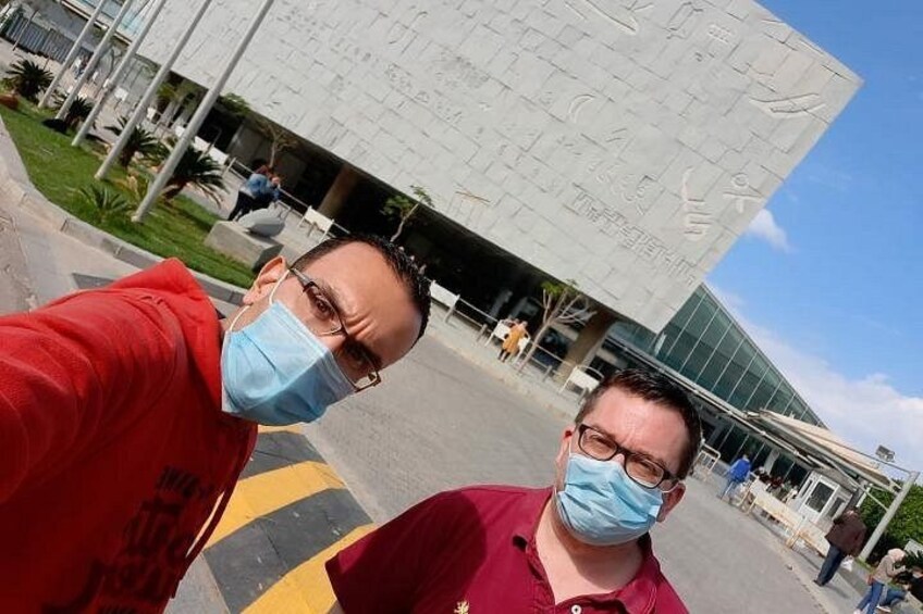 Dos personas tomándose un selfie frente a un edificio moderno con grandes inscripciones. 3
