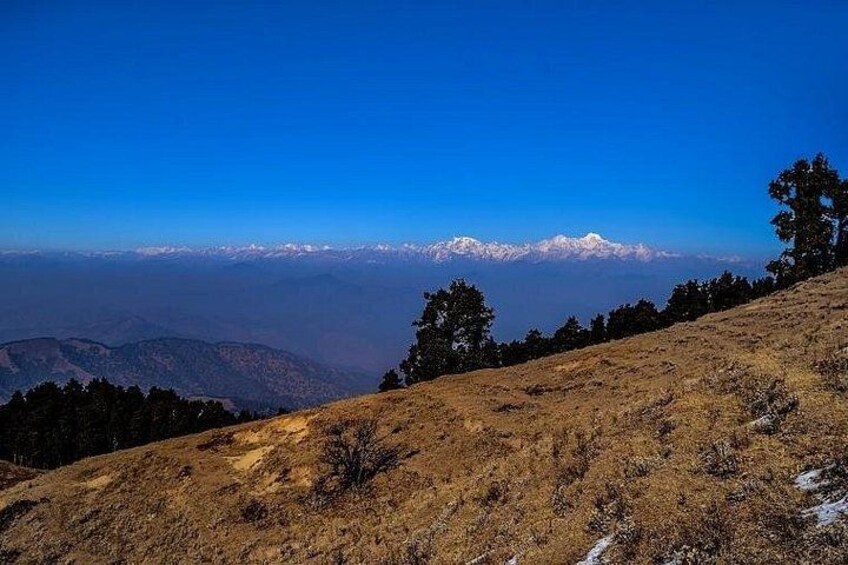 A mountainous landscape with a clear sky, a distant snow-capped mountain range, and sparse vegetation. 2